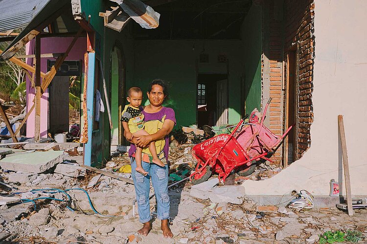 Frau mit Kind vor Ruine eines Hauses