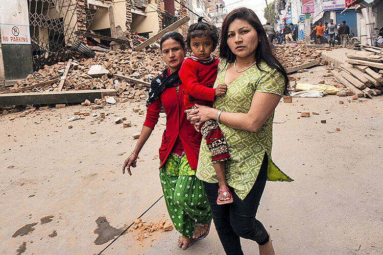 Zwei Frauen mit Kind vor Trümmern