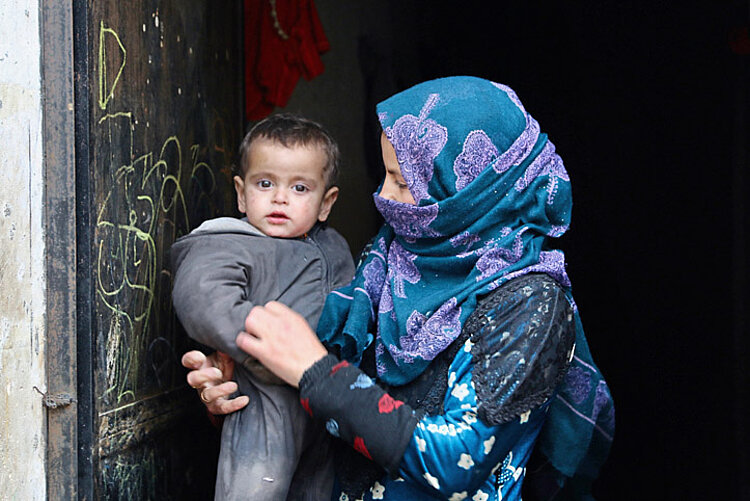 Eine verschleierte Frau steht vor einer Tür und hält ein kleines Kind im Arm
