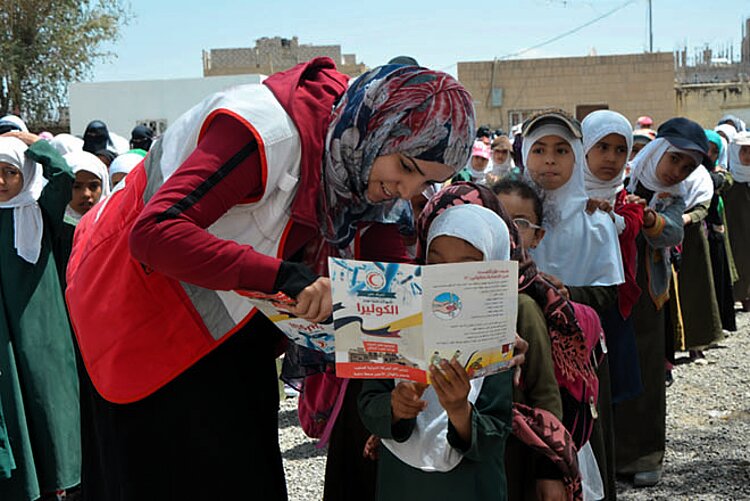 Kindern im Jemen helfen: Helferin des Jemenitischen Roten Halbmonds zeigt einem Mädchen einen Flyer