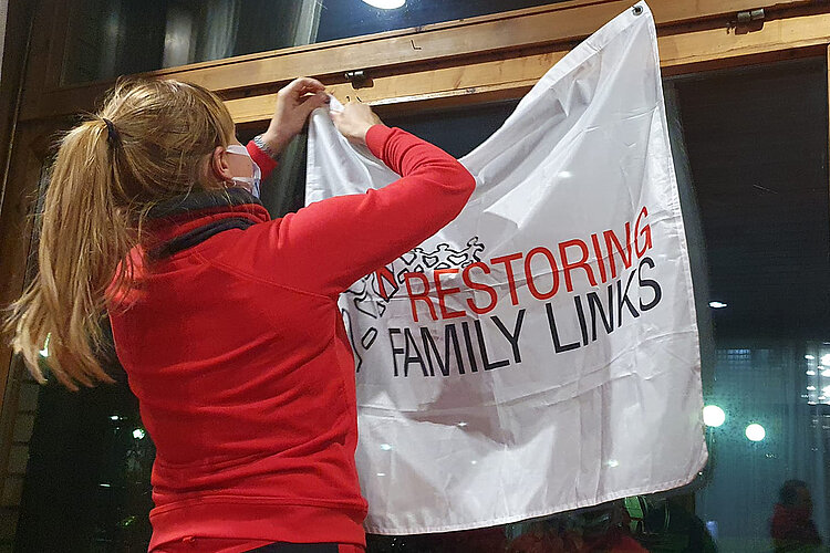 Rotkreuzlerin hängt Banner der internationalen Suchdienstes auf