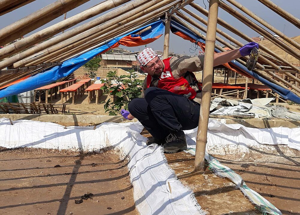 Ein Mann hockt im Lager Kutupalong unter einem Zelt und hält eine Abwasserprobe hoch
