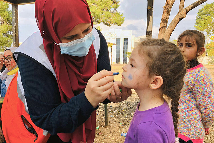 Freiwillige schminkt ein Mädchen 