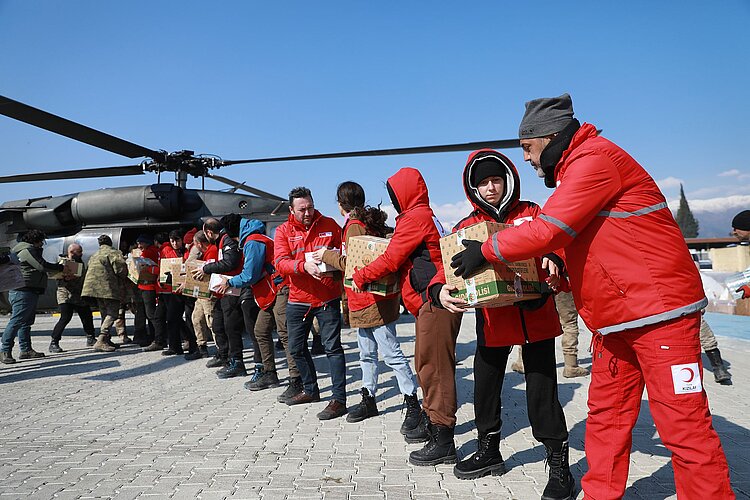 Kette von Helfenden entladen einen Helikopter mit Hilfsgütern.