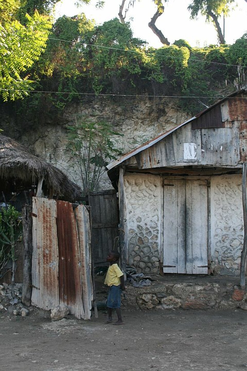 Foto: Ein typisches Haus auf Haiti, verstärkt durch rostiges Wellblech, davor ein Kind