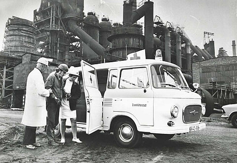 Im Stahlwerk Eisenhüttenstadt bringen Helfer einen verletzten Arbeiter zum Einsatzfahrzeug, um 1970 (Ilop / DRK)