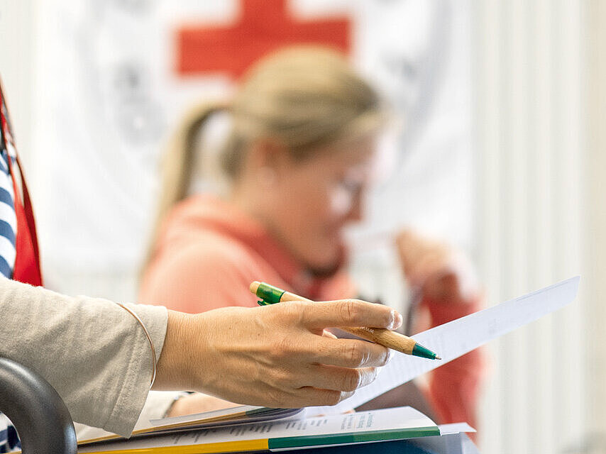 Foto: Zwei Frauen über Unterlagen gebeugt - im Hintergrund das DRK-Logo