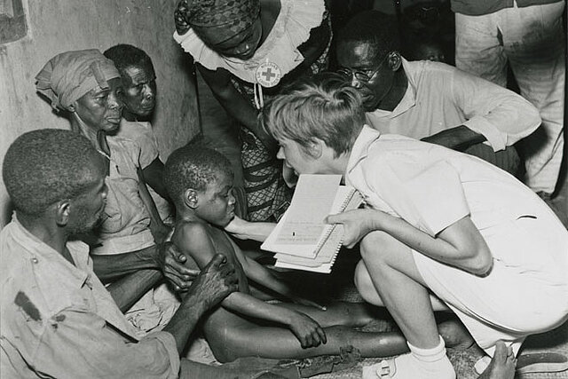 Foto: Rotkreuzkrankenschwester beugt sich zu einem nigerianischen Kind