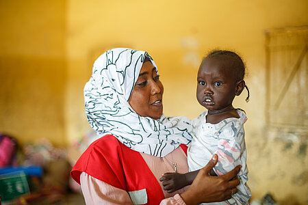 Bewaffneter Konflikt im Sudan: Freiwillige vom Sudanesischen Roten Halbmond mit einem Kleinkind von Binnenflüchtlingen auf dem Arm