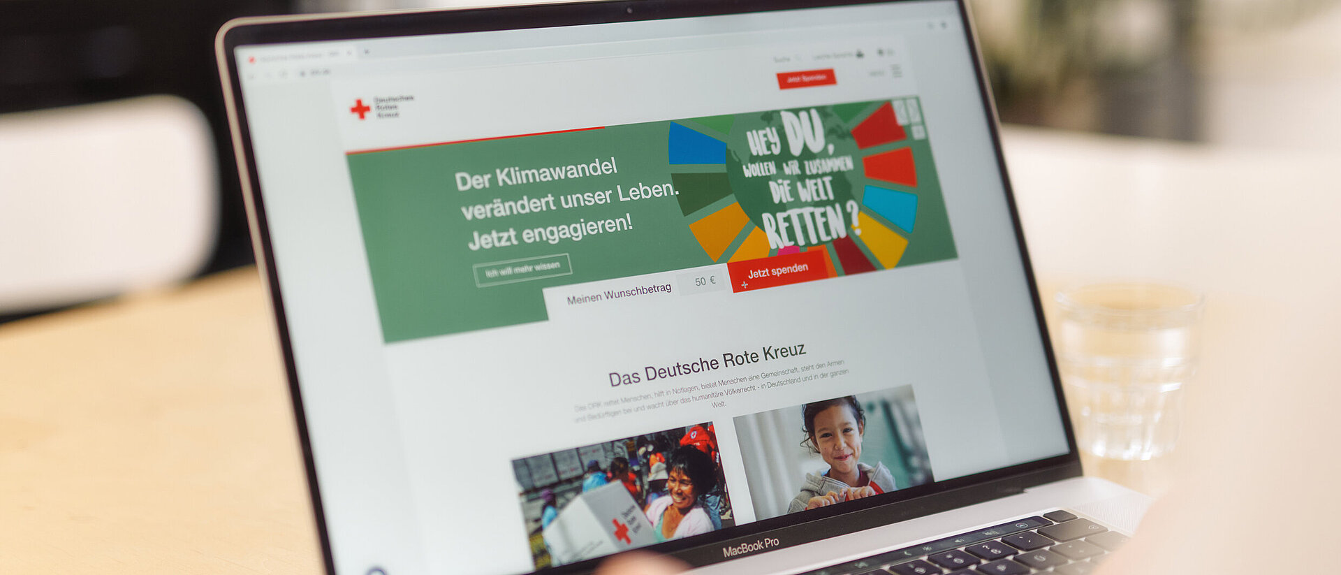 Auf einem Laptop ist eine Webseite des DRK zu sehen. Der Laptop steht auf einem Tisch, eine Person sitzt davor und nutzt den Laptop