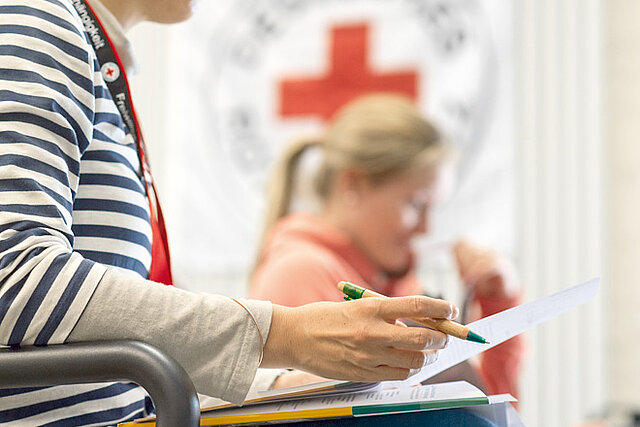 Foto: Zwei Frauen über Unterlagen gebeugt - im Hintergrund das DRK-Logo