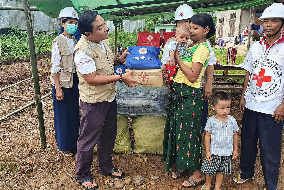 Frau mit Baby erhält Hilfsgüter von Rotkreuzler