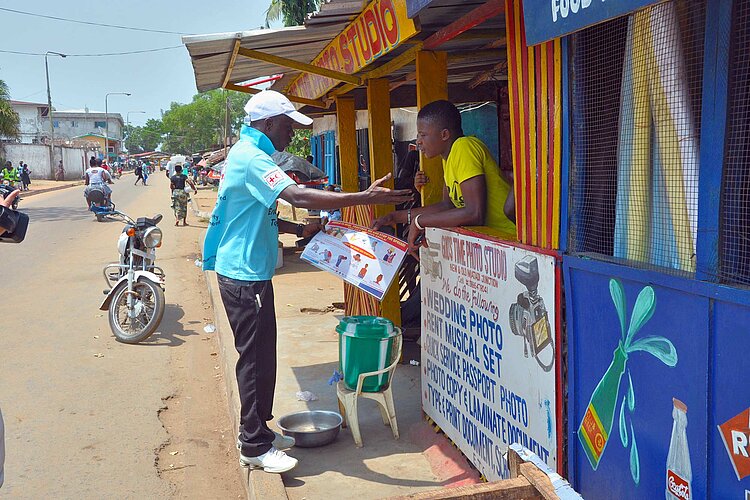 Rotkreuzler spricht mit Mann an Kiosk