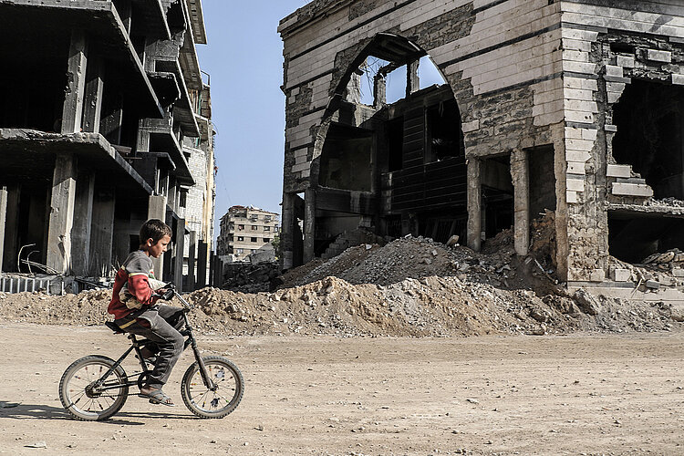 Syrischer Junge fährt zwischen Ruinen Fahrrad
