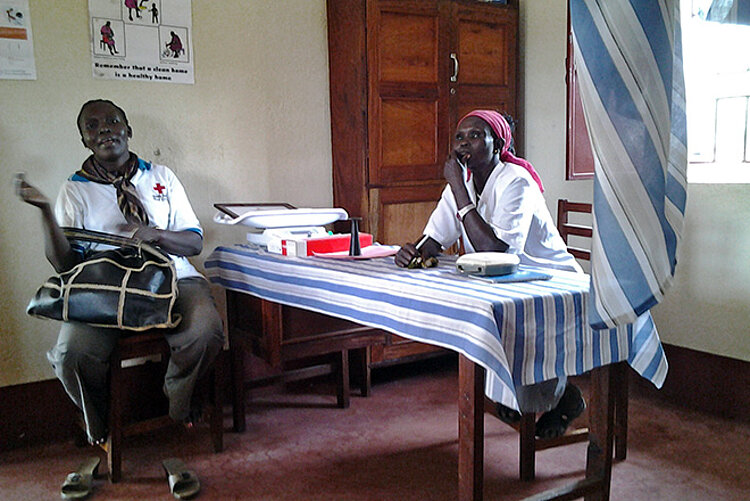 Zwei Personen des Roten Kreuzes sitzen in einer Gesundheitsstation am Tisch