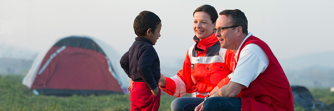 Foto: DRK-Mitarbeiter mit einem Flüchtlingskind vor einem Zelt in Griechenland.