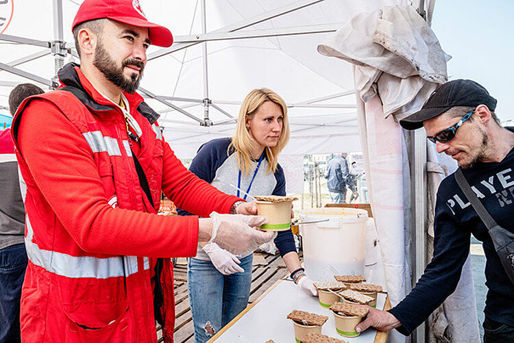 Zwei Rotkreuz-Helfende verteilen Suppe mit Knäckebrot