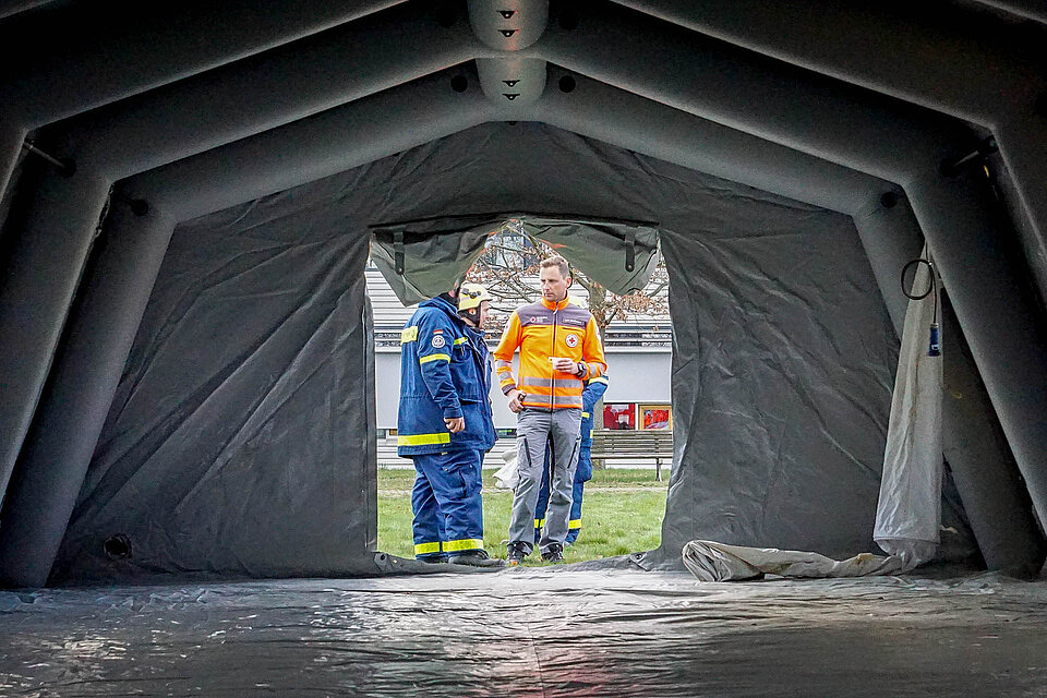 Ehrenamtlicher des DRK und Helfer des THW vor leerem Zelt der Notfallambulanz