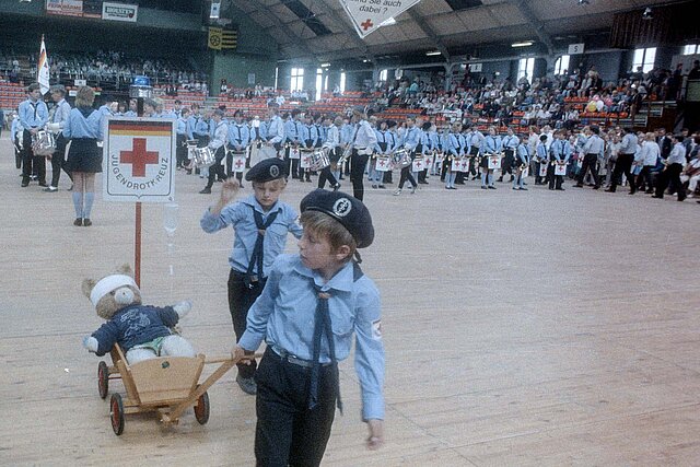 Kinder in JRK-Uniformen mit Teddy im Bollerwagen