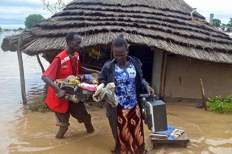 Helfer und Frau vor überschwemmter Hütte