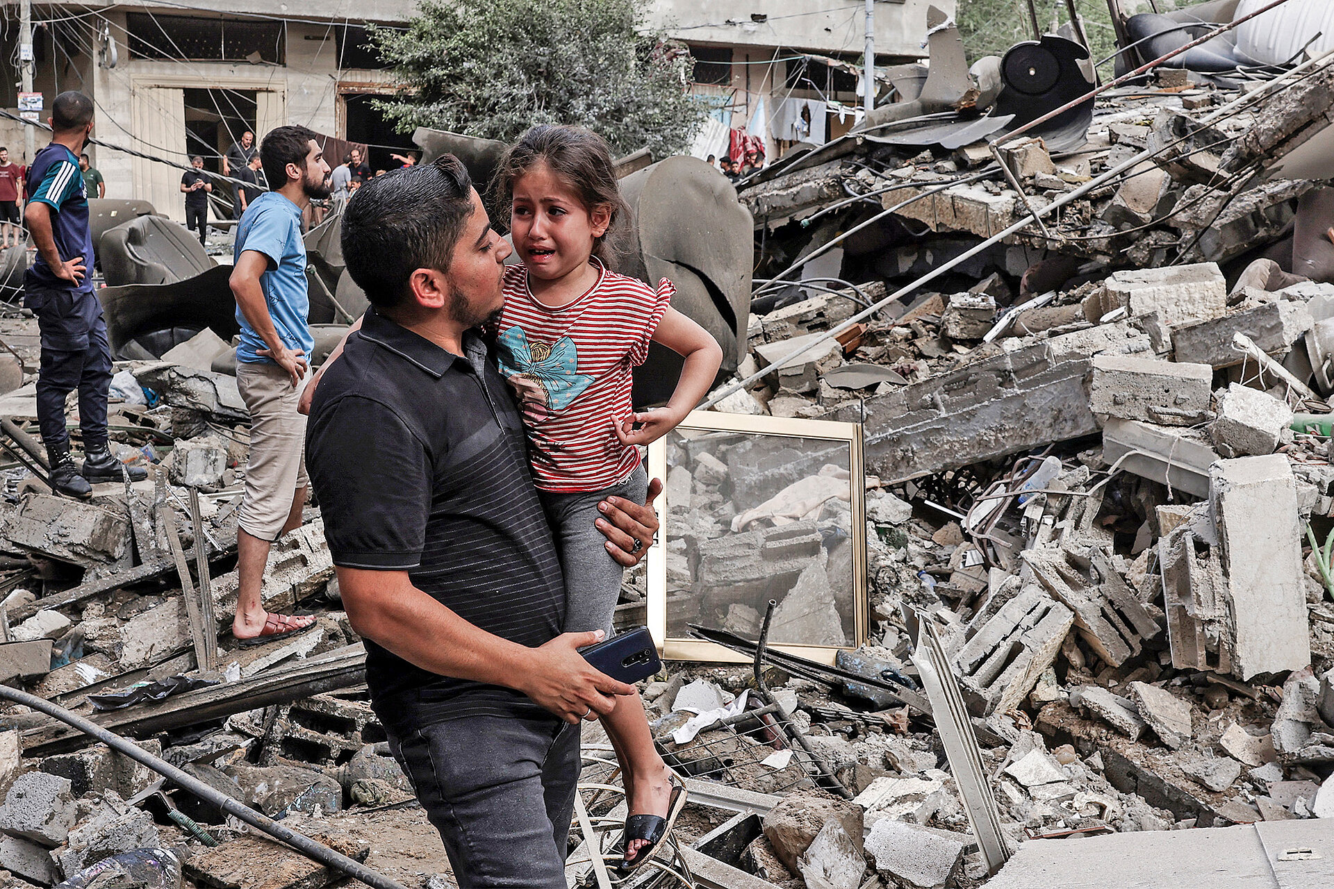 Ein Mann trägt ein Kind vor zerstörtem Gebaüde in Gaza am 7. Oktober 2023  