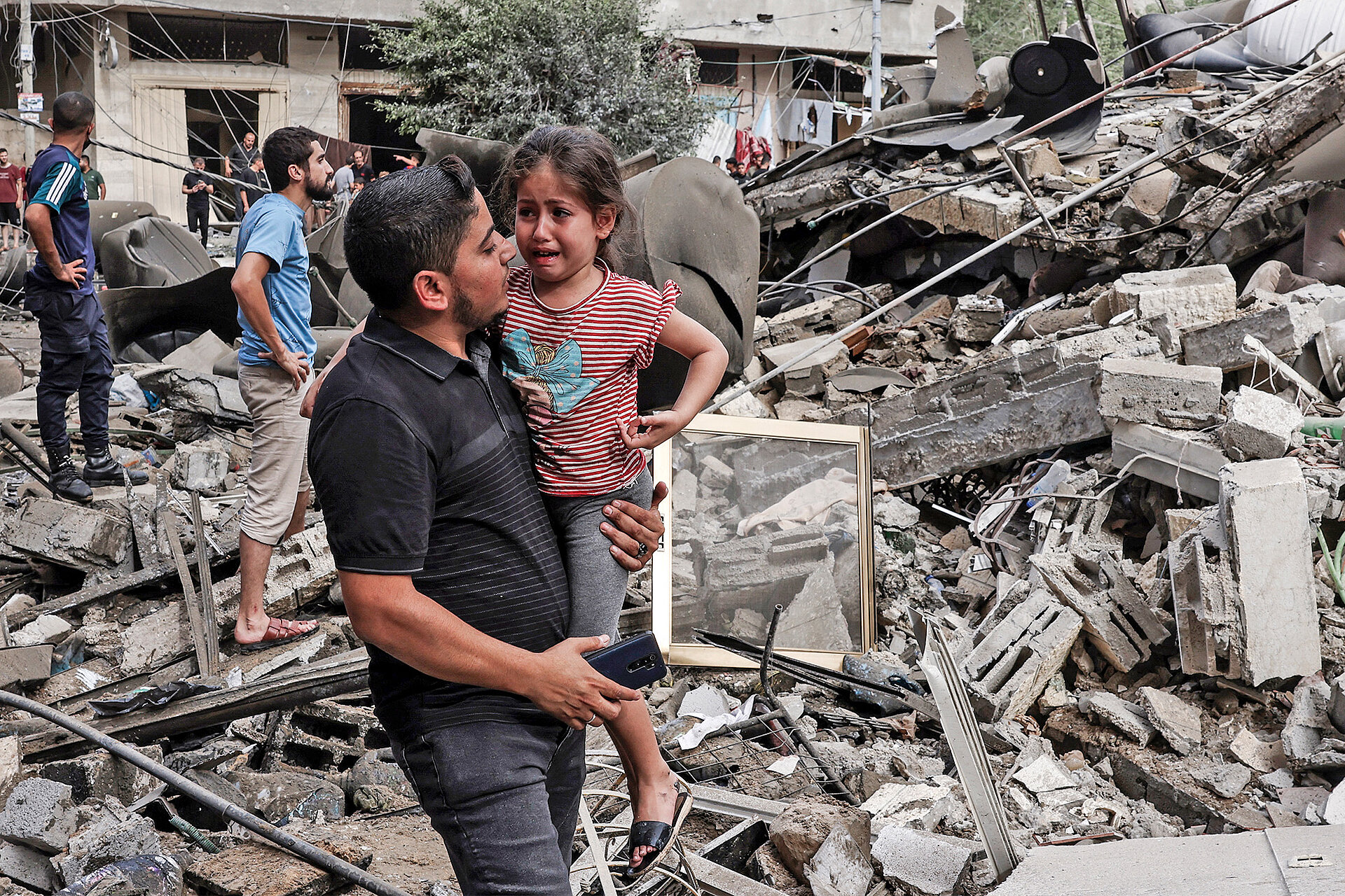 Ein Mann trägt ein Kind vor zerstörtem Gebaüde in Gaza am 7. Oktober 2023  