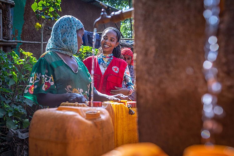 Frau und Helferin sprechen am Brunnen