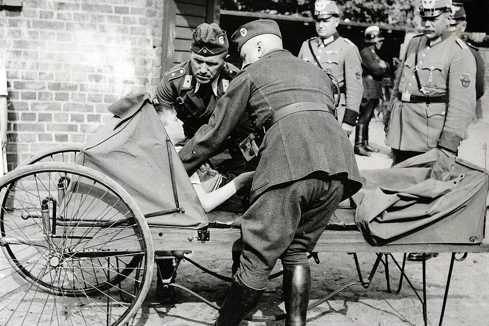DRK-Helfer legt Schüler auf fahrbare Trage