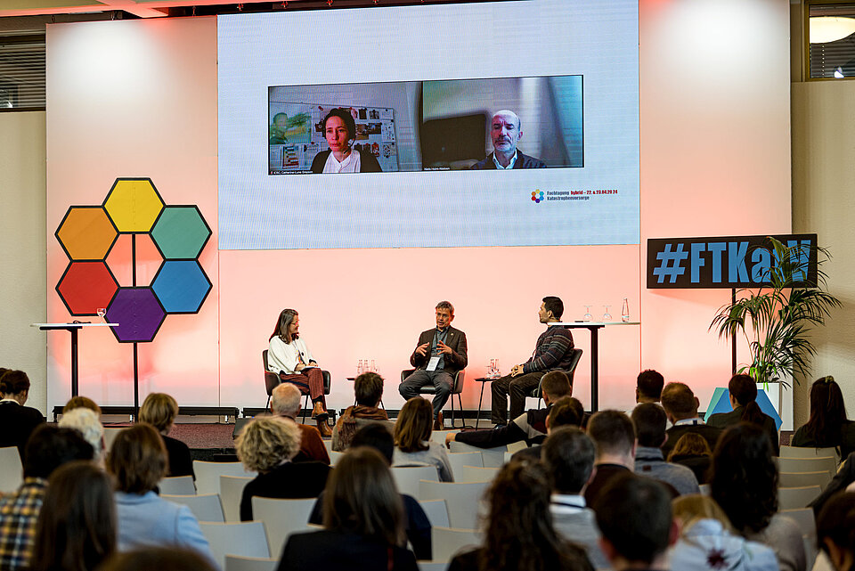Hybrides internationales Panel mit drei Personen auf dem Podium und zwei Personen auf dem Bildschirmnce"