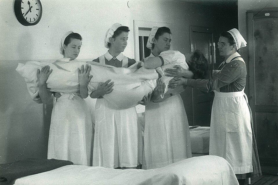 DRK-Schwesternhelferinnen heben eine Patientin