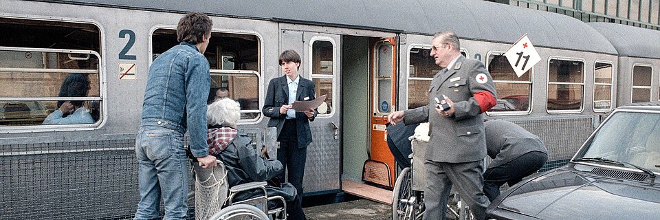 Rollstuhlfahrer und Helfer vor Zug