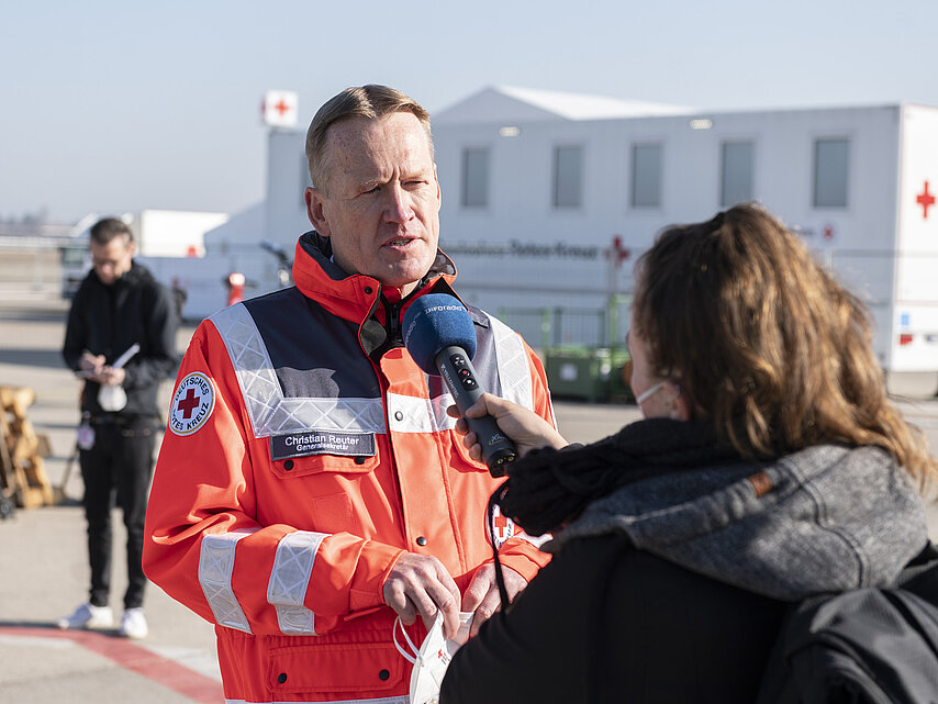 DRK-Generalsekretär Christian Reuter steht in DRK-Einsatzkleidung im Freien und wird von einer Frau interviewt