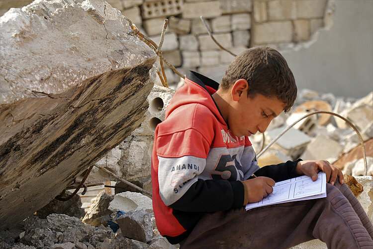 Junge arbeitet zwischen Trümmern in einem Buch