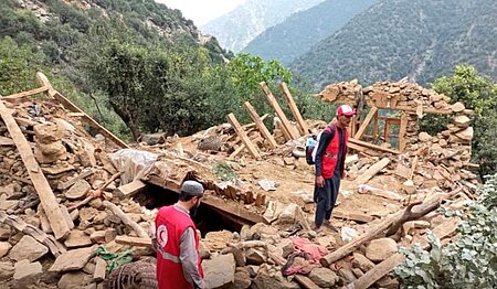 Helfende des Afghanischen Roten Halbmonds auf Trümmern von zerstörten Häusern.