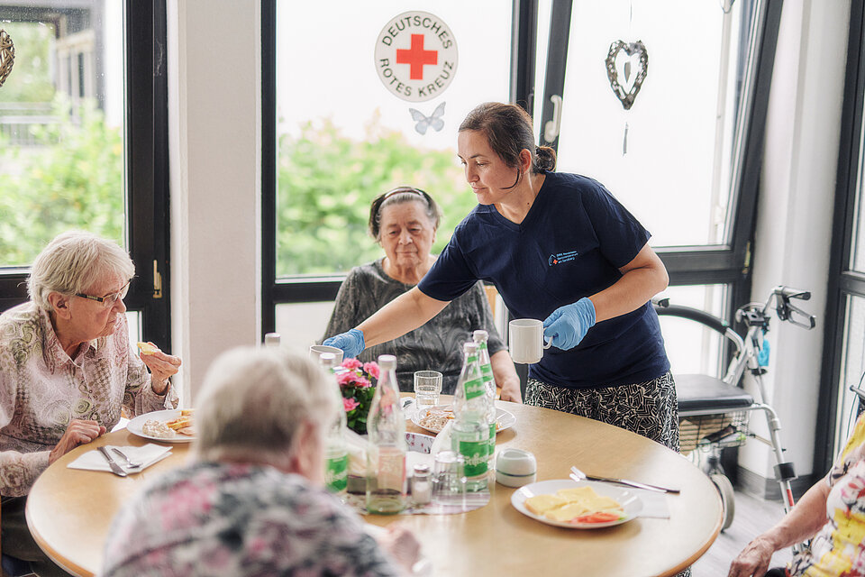 DRK-Mitarbeiterin teilt Essen aus an eine Gruppe von älteren Menschen