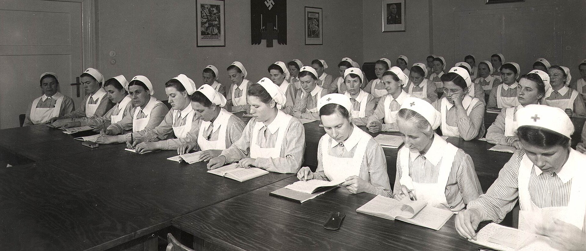 Schwesternhelferinnen an Bänken - Hakenkreuz an Wand
