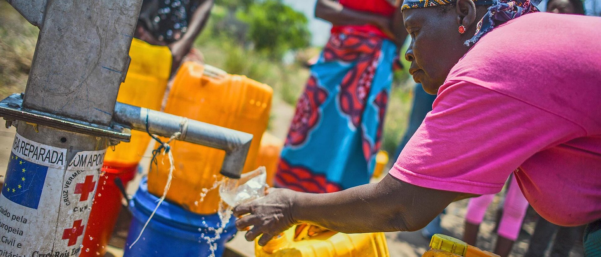 Frau gießt an Wasserstelle Wasser in Glas