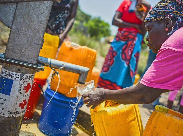 Frau gießt an Wasserstelle Wasser in Glas