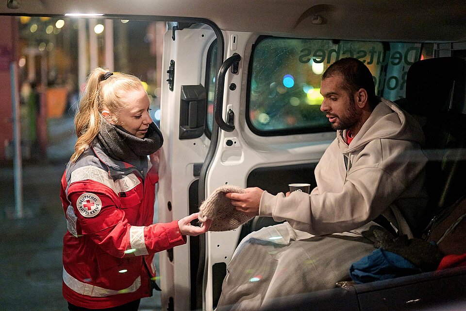 Ehrenamtliche reicht Mann im Wärmebus Mütze