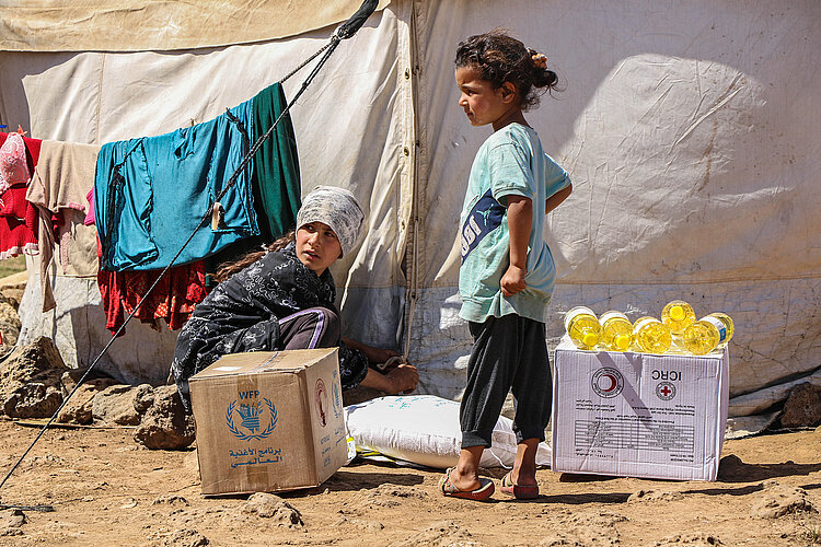 Syrische Kinder mit Hilfsgüter vor Zelt