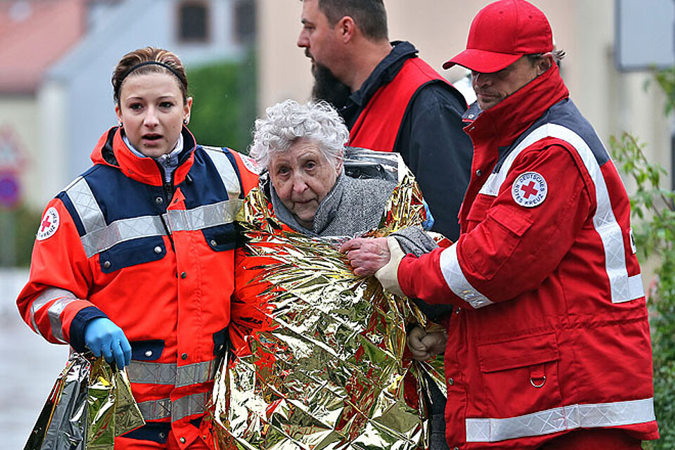 Seniorin mit Rettungsdecke und zwei DRK-Ehrenamtlichen