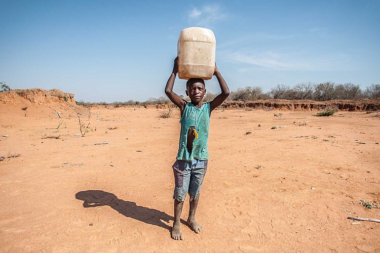 Dürre in Mosambik Junge mit Wasserkanister vor Wüste