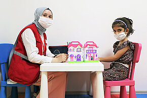 Türkische Rothalbmond-Helferin mit syrischem Mädchen am Tisch