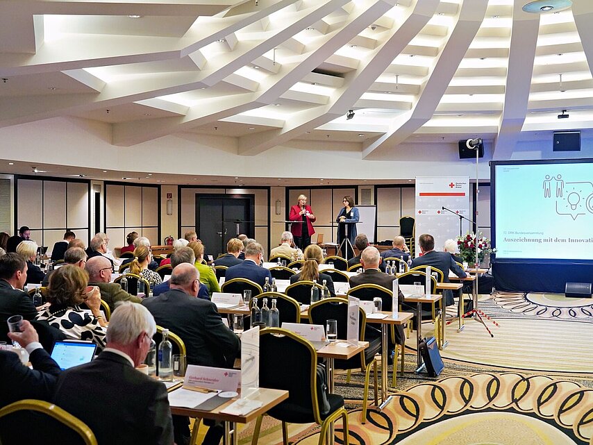 Verleihung des DRK - Innovationspreises 2023 im Rahmen der Bundesversammlung: DRK - Vizepräsidentin Ulrike Würth und Gisela Wedler (Teamleiterin im Bereich Jugend und Wohlfahrt beim DRK-Generalsekretariat) vor den Teilnehmern.