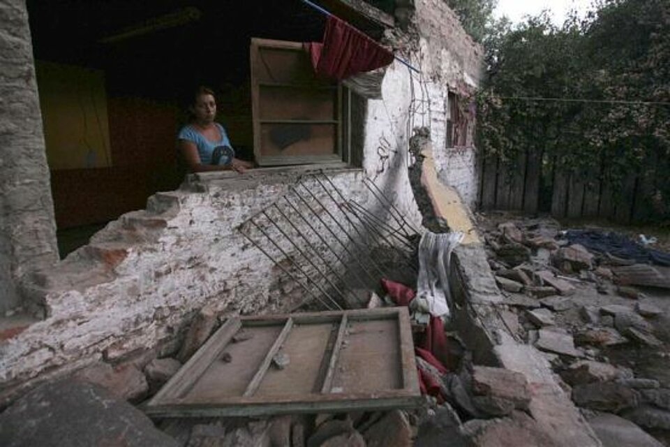 Foto: eine Frau schaut aus ihrem beschädigtem Haus.