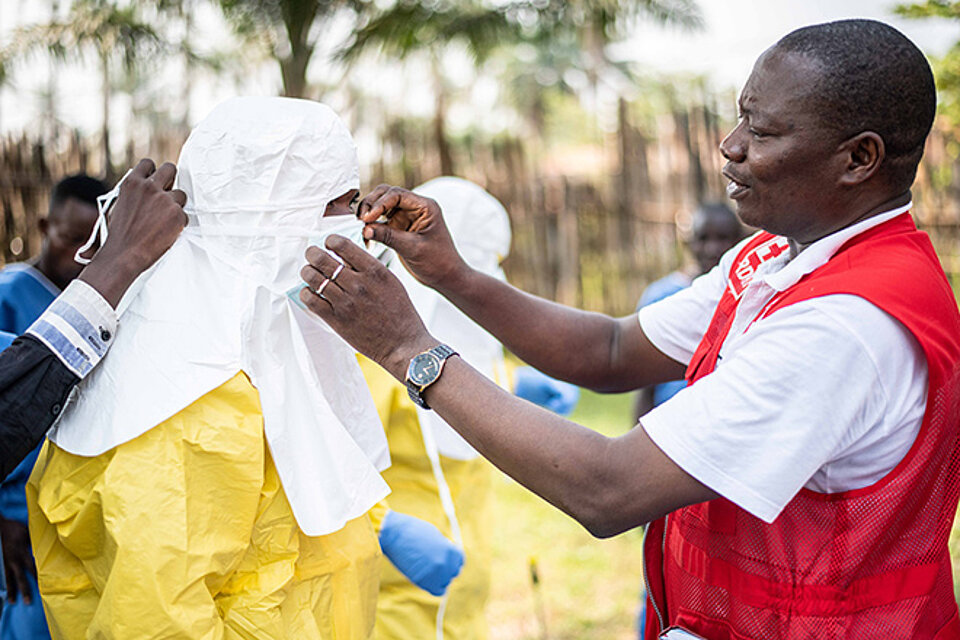 Foto: Kongolesischer Rotkreuzler hilft einem Mann beim Anlegen der Ebola-Schutzkleidung 