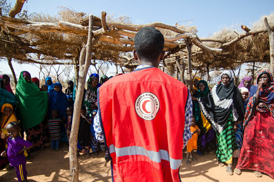 Foto: Rothalbmondhelfer in Somalia steht vor einer Gruppe von Frauen und Kindern