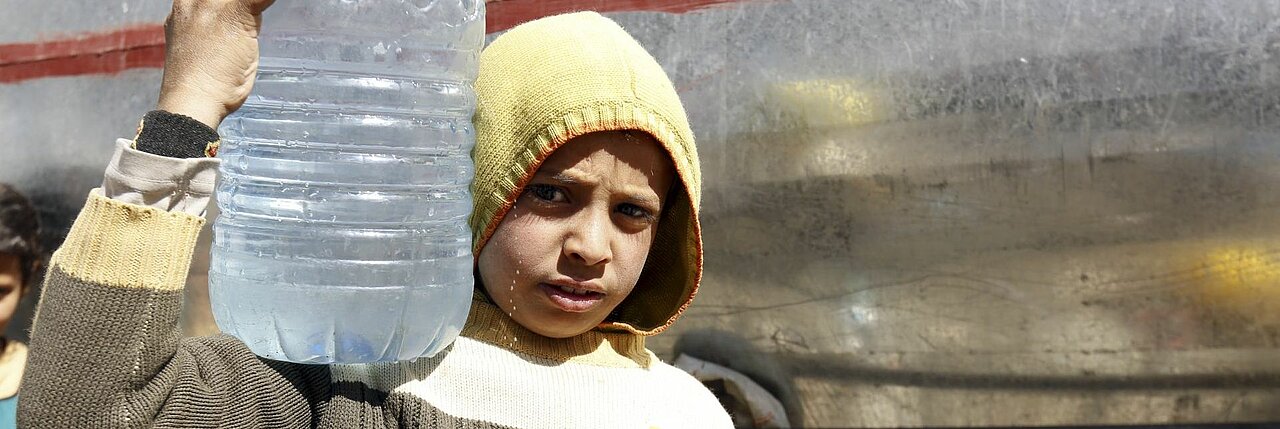 Junge im Konfliktgebiet trägt eine Flasche mit Trinkwasser