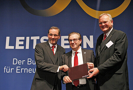 Foto: Matthias Platzeck, Jan Hofer und Dirk U. Hindrichs auf der Bühne. Jan Hofer hält ein Solarmodul in der Hand