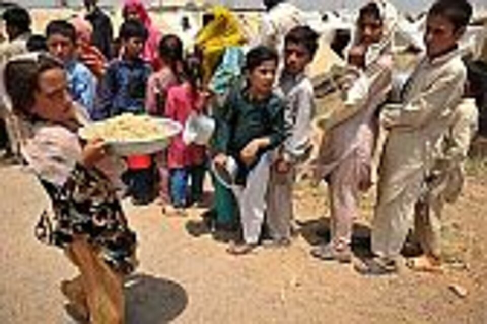 Foto: Flüchtlingskinder in Pakistan stehen Schlange für in warmes Essen, im Vordergrund ein junges Mädchen, das einen bereits gefüllten Teller trägt